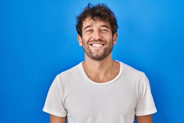 西班牙裔年轻人站在蓝色的背景上 脸上挂着快乐而沉着的微笑 幸运的人 — 图库照片