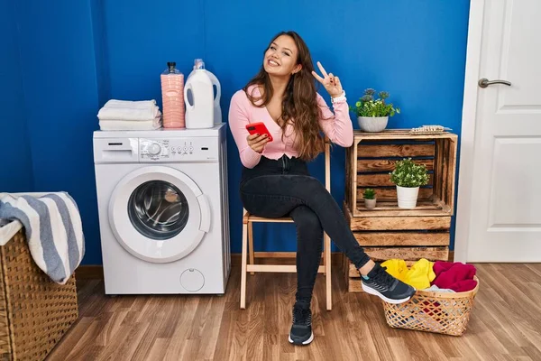 Mujer Hispana Joven Sentada Esperando Lavandería Usando Teléfono Inteligente Sonriendo —  Fotos de Stock