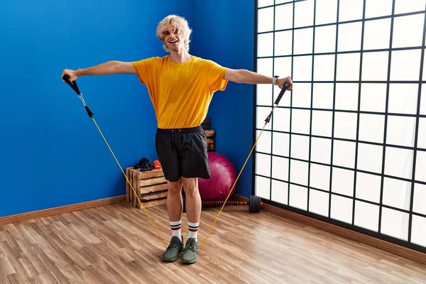 Young blond man smiling confident using elastic band training at sport center