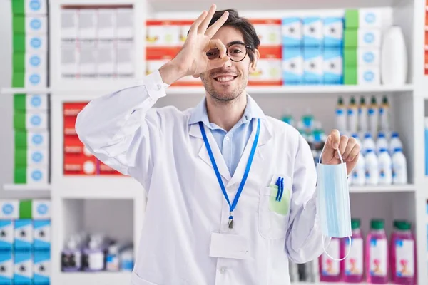 Young Hispanic Man Working Pharmacy Drugstore Holding Safety Mask Smiling — Foto de Stock