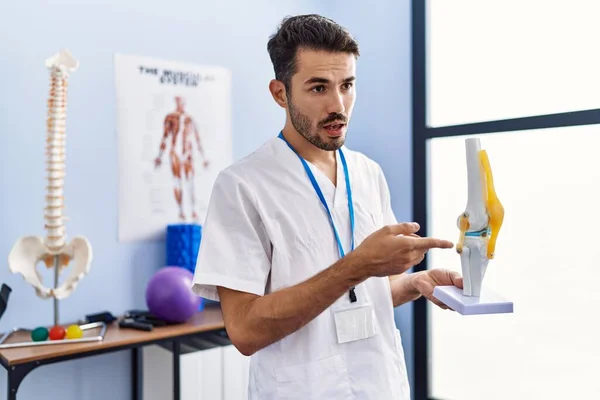 Mladý Hispánec Uniformě Fyzioterapeuta Drží Anatomický Model Kolena Rehabilitační Klinice — Stock fotografie