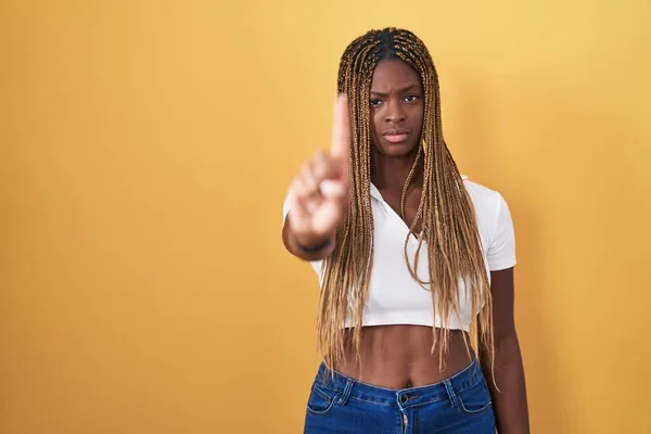 アフリカ系アメリカ人の女性で 髪の毛が黄色い背景の上に立ち 指を上げて怒りの表情で指摘し ジェスチャーを示さない — ストック写真