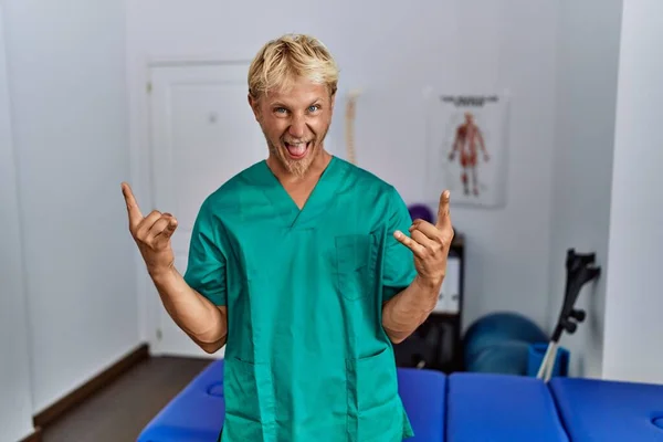 Young Blond Man Wearing Physiotherapist Uniform Standing Clinic Shouting Crazy — Stockfoto