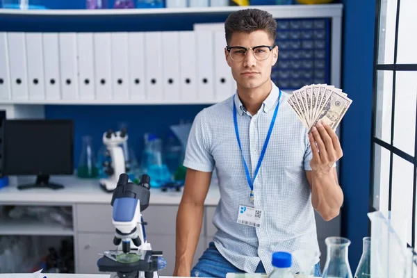 Joven Hombre Hispano Trabajando Laboratorio Científico Sosteniendo Dólares Pensando Actitud — Foto de Stock