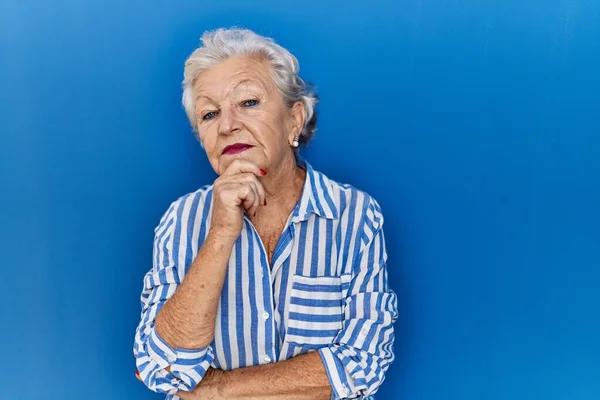 Starsza Kobieta Siwymi Włosami Stojąca Nad Niebieskim Tłem Ręką Podbródku — Zdjęcie stockowe