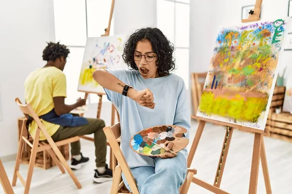 Young hispanic woman at art studio looking at the watch time worried, afraid of getting late