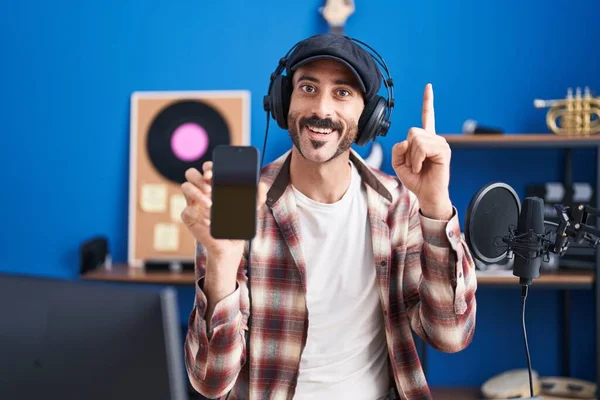 Hombre Hispano Con Barba Estudio Música Mostrando Smartphone Sorprendido Con — Foto de Stock