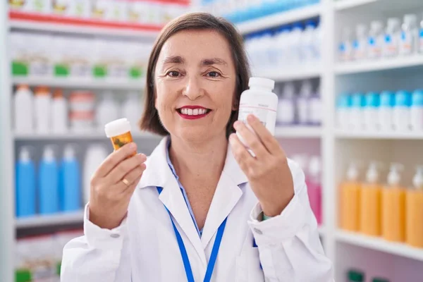 Mujer Mediana Edad Farmacéutico Sonriendo Confiado Sosteniendo Pastillas Botellas Farmacia — Foto de Stock