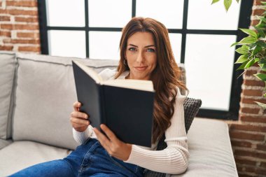 Evdeki kanepede oturmuş kitap okuyan genç İspanyol kadın.