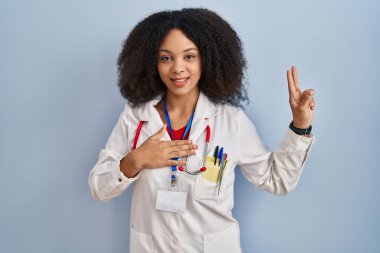 Genç Afro-Amerikan kadın doktor üniforması ve steteskop ile gülümsüyor. Göğsü ve parmakları havada yemin ediyor. Sadakat yemini ediyor. 