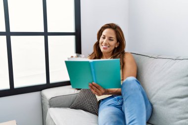 Genç Latin kadın evde çay içip kitap okuyor.