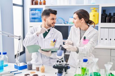 Man and woman wearing scientist uniform writing on notebook at laboratory