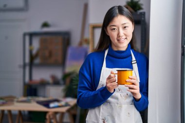 Resim stüdyosunda kahve içen kendine güvenen Çinli bir sanatçı.