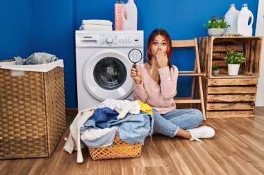 Genç beyaz kadın büyüteç kullanıyor kirli çamaşırlarda leke arıyor ağzını eliyle kapatıyor, şok geçiriyor ve hata yapmaktan korkuyor. şaşırmış ifade 