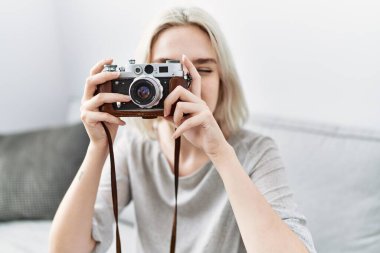 Beyaz bir kadın evde kamerayla gülümsüyor.