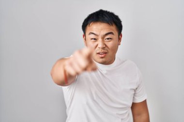 Young chinese man standing over white background pointing displeased and frustrated to the camera, angry and furious with you 