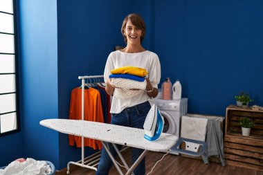 Brunette woman holding folded laundry after ironing celebrating crazy and amazed for success with open eyes screaming excited. 