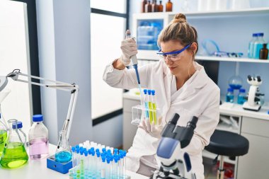 Laboratuvarda pipet kullanan bilim adamı üniforması giyen genç sarışın kadın.