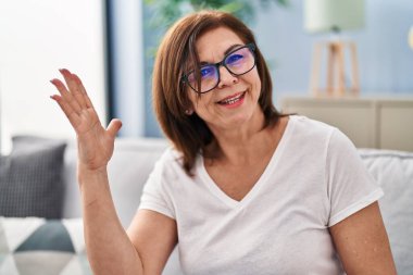 Orta yaşlı bir kadın koltukta oturmuş evde konuşuyor.