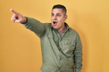 Sarı arka planda dikilen İspanyol genç adam parmağı önde, ağzı açık, şaşırmış bir ifade, ön tarafta bir şey. 
