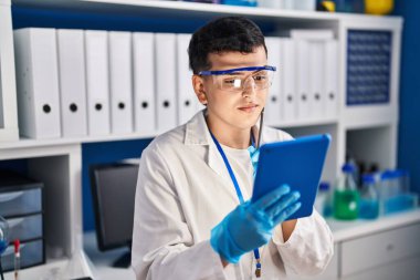 Young non binary man scientist using touchpad at laboratory