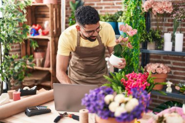 Young arab man florist using laptop holding plant at florist