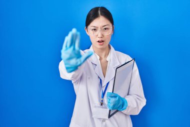 Laboratuvarda çalışan Çinli genç bir kadın avuç içleriyle jestleri durduruyor. Öfkeli ve hayal kırıklığı dolu bir ifade. 