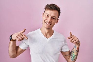 Caucasian man standing over pink background looking confident with smile on face, pointing oneself with fingers proud and happy. 