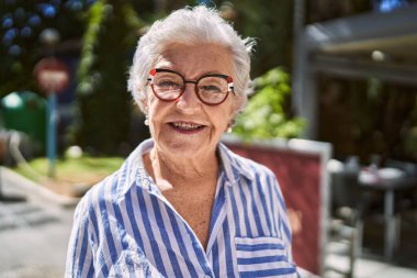 Yaşlı, kır saçlı, gülümseyen bir kadın sokakta kendine güveniyor.