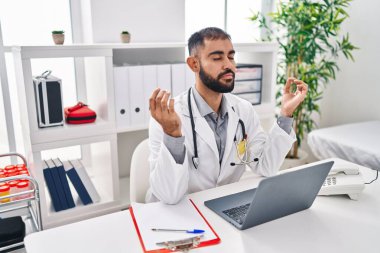Young hispanic man doctor doing yoga exercise at clinic