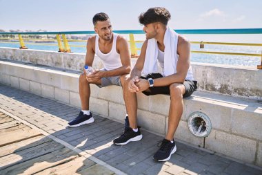 İki İspanyol erkek, gülümseyen bir çift, deniz kenarında bankta oturuyorlar.