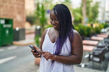 Afro-Amerikalı bir kadın kahve dükkanının terasında akıllı telefon kullanarak gülümsüyor.