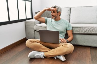 Orta yaşlı, İspanyol bir adam oturma odasında dizüstü bilgisayar kullanıyor. Çok mutlu ve gülümsüyor. Başını kaldırıp uzaklara bakıyor. arama kavramı. 