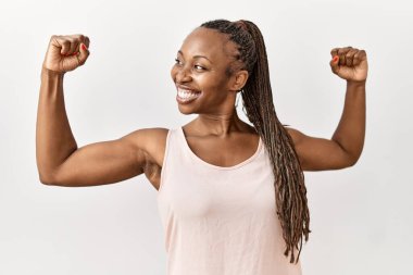 Örgülü siyah kadın izole edilmiş arka planda duruyor ve gururla gülümseyen kol kaslarını gösteriyor. fitness konsepti. 