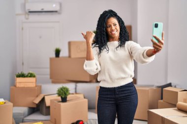Orta yaşlı İspanyol kadın yeni evine taşınıyor. Selfie çekiyor. Parmağını yana kaldırıyor, ağzı açık gülümsüyor. 