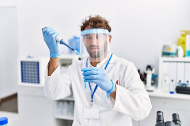 Laboratuvarda çalışan, bilim adamı üniforması giyen İspanyol genç adam.