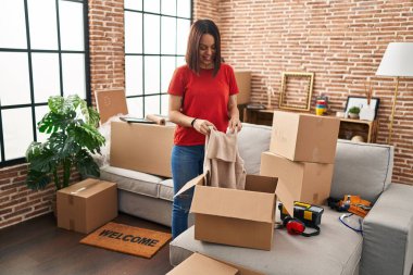 Genç, güzel, İspanyol bir kadın gülerek yeni evindeki karton kutuları açıyor.