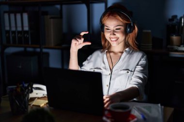Geceleri büroda çalışan beyaz bir kadın gülümsüyor ve el hareketleriyle hareket ediyor. Küçük boy işareti yapıyor, parmakları bakıyor ve kameraya bakıyor. ölçüm kavramı. 