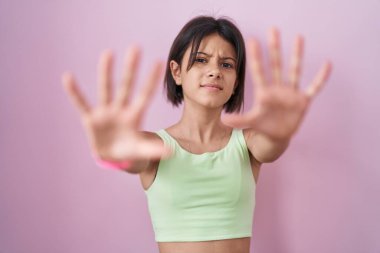 Pembe arka planda duran genç kız avuçlarıyla jestleri durduruyor, kızgın ve hayal kırıklığı dolu bir ifade takınıyor. 