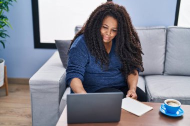 African american woman using laptop reading notebook at home