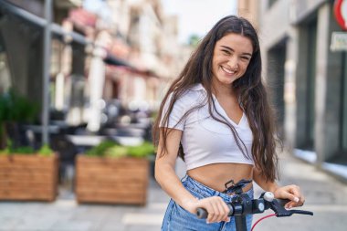 Young hispanic woman smiling confident using e-scooter at street