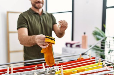 Orta yaşlı İspanyol adam çamaşırhanede çamaşır ipine kıyafet asıyor.