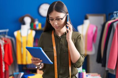 Çinli kadın terzi akıllı telefondan dikiş atölyesinde dokunmatik ped kullanarak konuşuyor.
