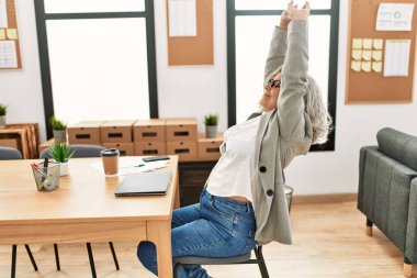 Orta yaşlı, kır saçlı iş kadını ofiste çalışırken kollarını esnetmekten yoruldu..