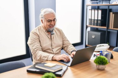 Ofiste çalışırken dizüstü bilgisayar kullanan orta yaşlı, kır saçlı bir iş adamı.