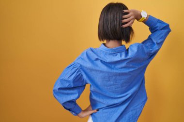 Sarı arka planda duran genç kız, elleri başının üstünde şüpheyi düşünüyor. 