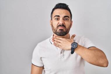 Beyaz arka plan üzerine gündelik giysiler giymiş, boğazını bıçak niyetine kesen, saldırganlığı şiddet ile tehdit eden Latin kökenli genç bir adam. 