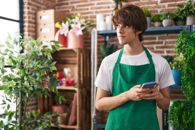 Çiçekçide akıllı telefon kullanan genç sarışın bir çiçekçi.