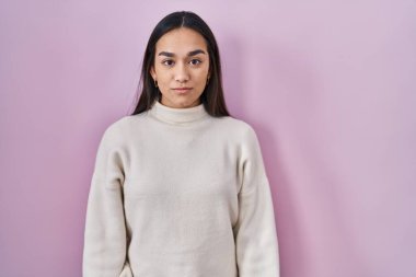 Pembe arka planda duran genç Güney Asyalı kadın yüzünde ciddi bir ifadeyle rahatlamış. Basit ve doğal bir şekilde kameraya bakıyorsun.. 