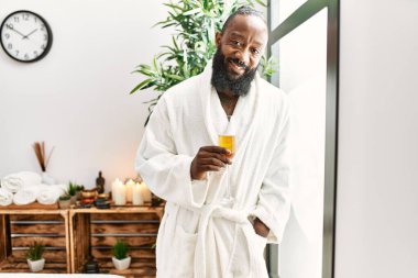 Genç Afro-Amerikan adam kendine güvenen bir şekilde gülümsüyor güzellik merkezinde şampanya içiyor.